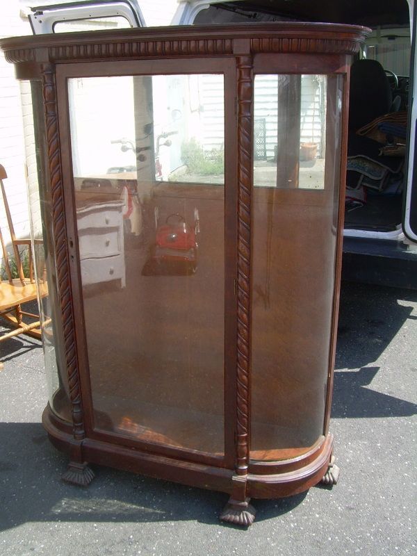 Antique wooden glass display cabinet with curved front, standing outdoors on pavement