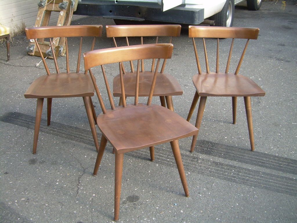 Four wooden chairs arranged outdoors on pavement, with a vintage look and one chair centered in front.