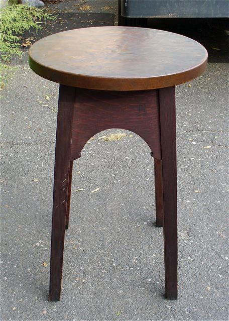 Tall wooden stool with a round top, shown outdoors on pavement.