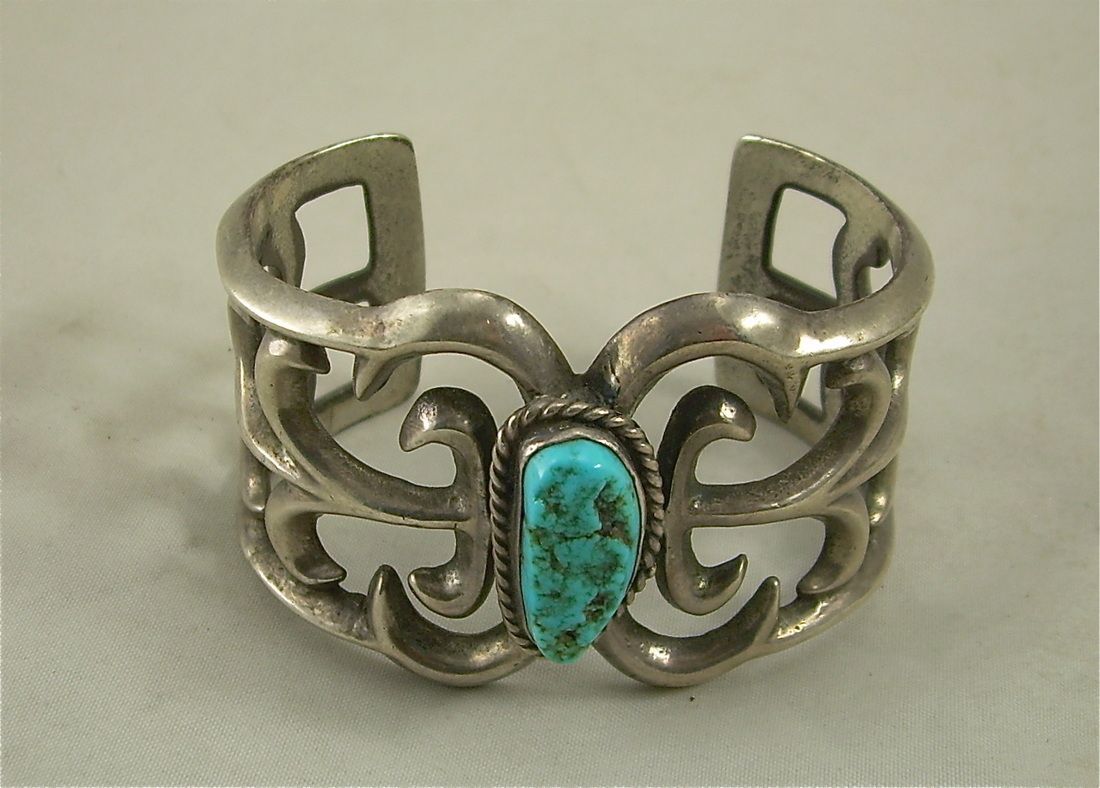 Silver cuff bracelet with ornate cutout design and a turquoise stone centerpiece