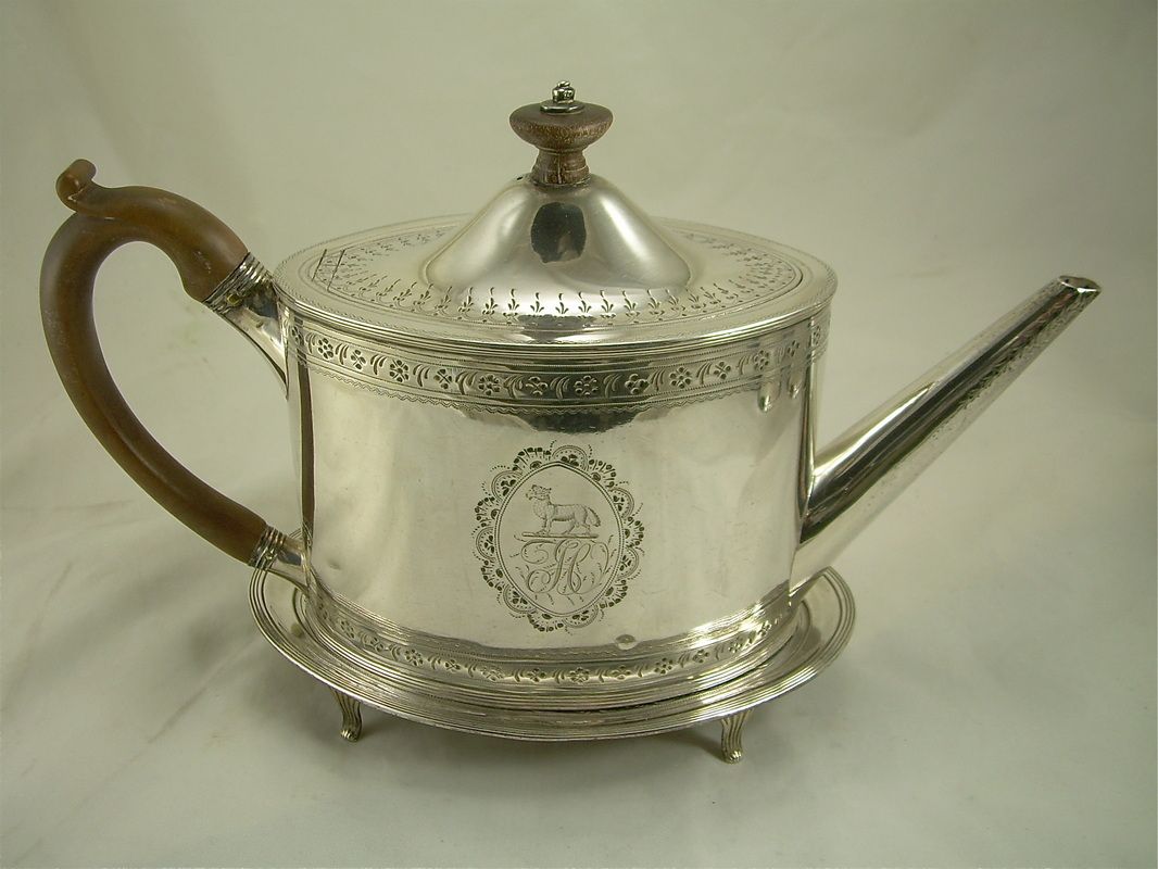 Silver teapot with lid, curved wooden handle, long spout, and engraved floral design