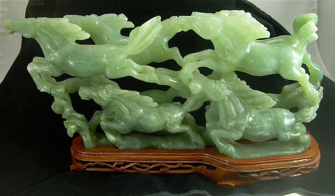 Green carved jade sculpture on an ornate wooden base against a dark background