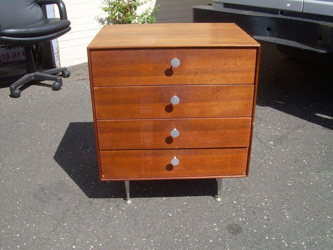 Small wooden four-drawer dresser on short legs, standing outdoors on pavement.