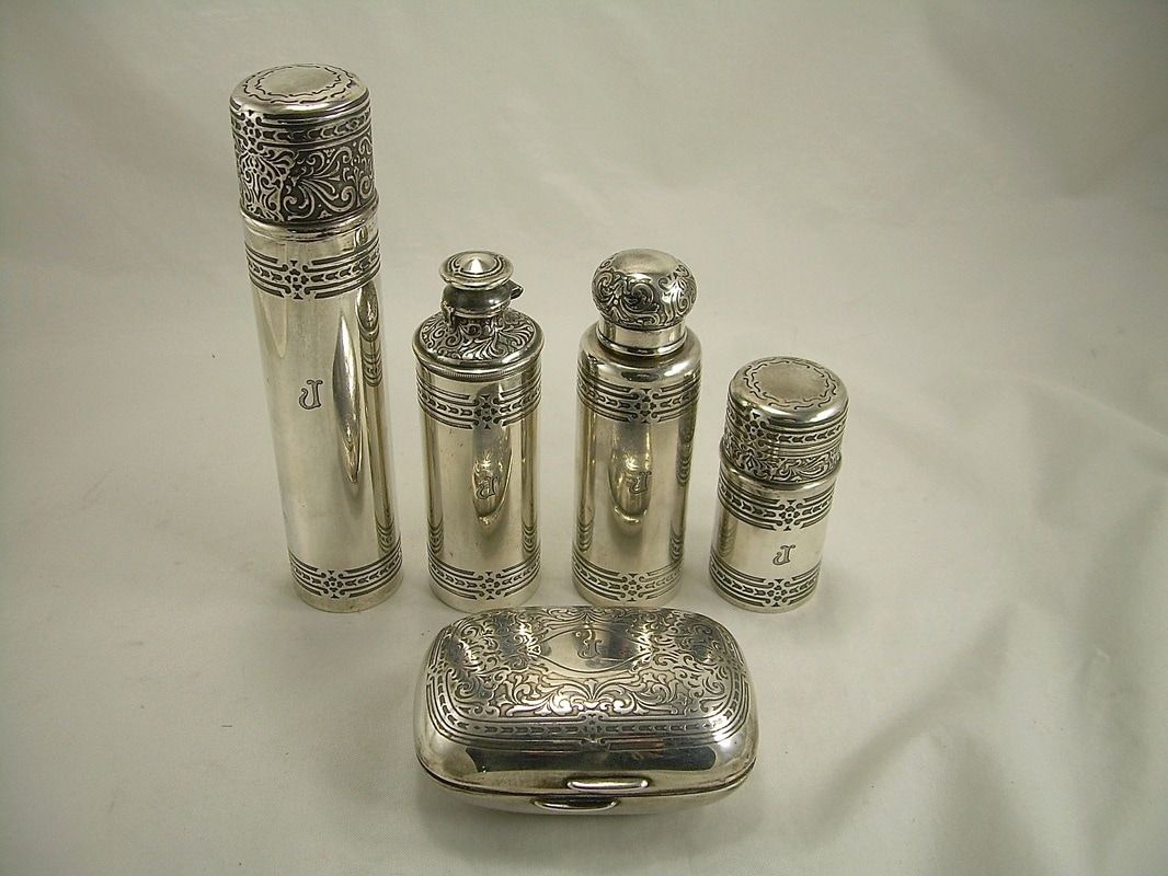 Five ornate silver containers and a matching tray on a light surface.