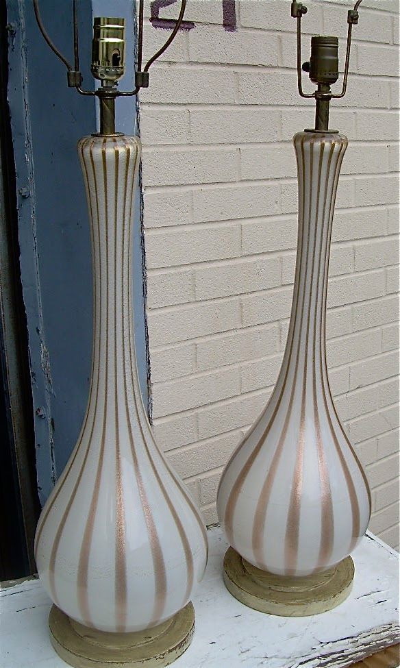 Two striped glass table lamps with bulbous bases and narrow necks on a shelf against a brick wall.
