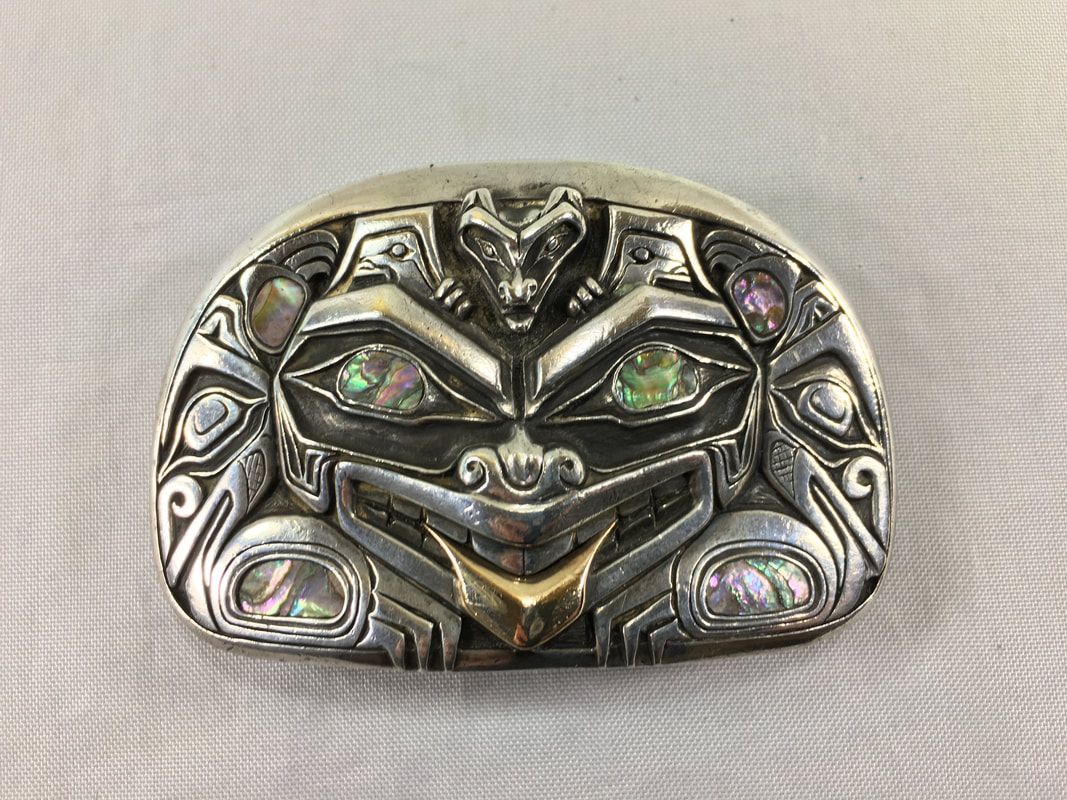 Silver-toned carved face brooch with iridescent inlaid stones on a light fabric background
