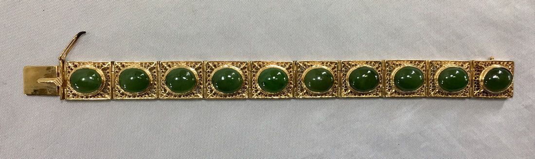 Gold bracelet with green oval gemstones and a small clasp on a light fabric background