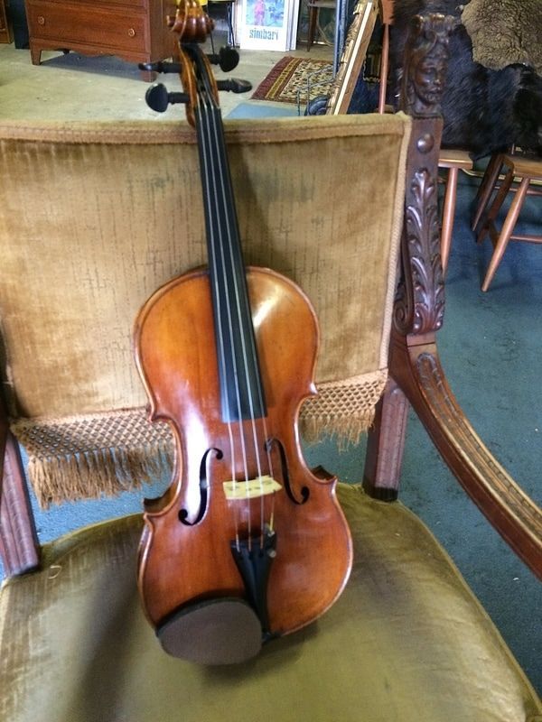 Violin with a dark fingerboard resting on a green upholstered chair in a music shop.