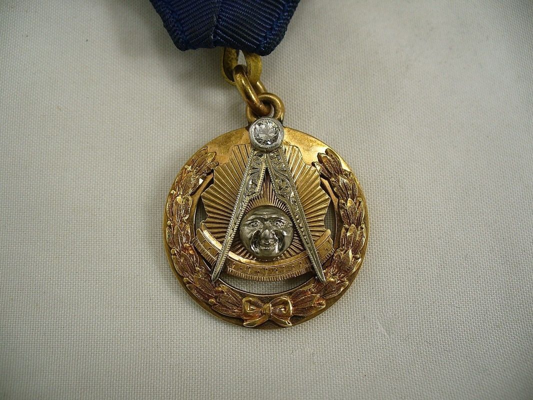 Gold medal pendant with a blue ribbon, featuring an emblem and laurel wreath design