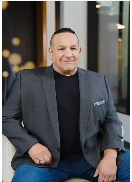 A man in a suit and black shirt is sitting on a couch.
