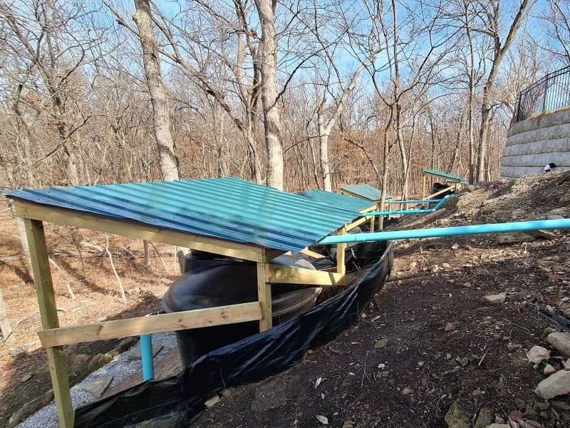 Residential rainwater harvesting system with collection barrels beside an Oklahoma home