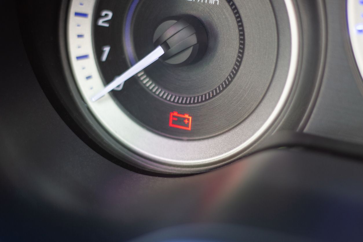 Car dashboard tachometer with a red low battery warning light illuminated