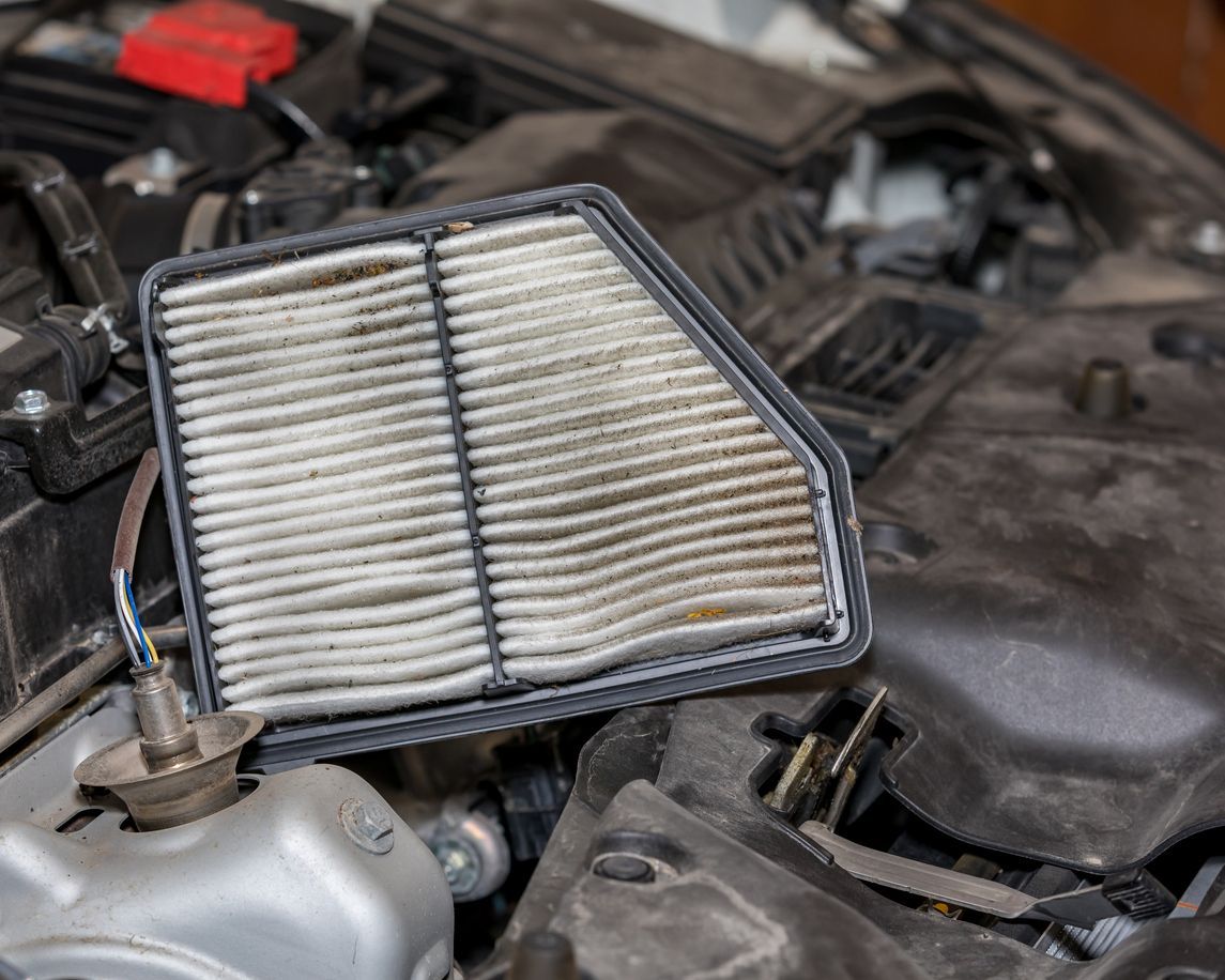Dirty car air filter removed from the engine bay, showing a clogged white pleated filter on a black frame.