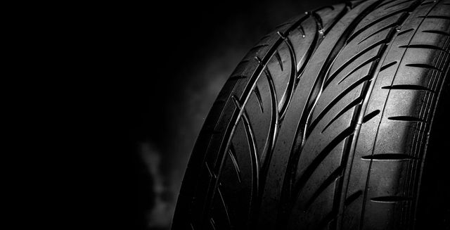 Close-up of a car tire tread on a dark background, lit from the side