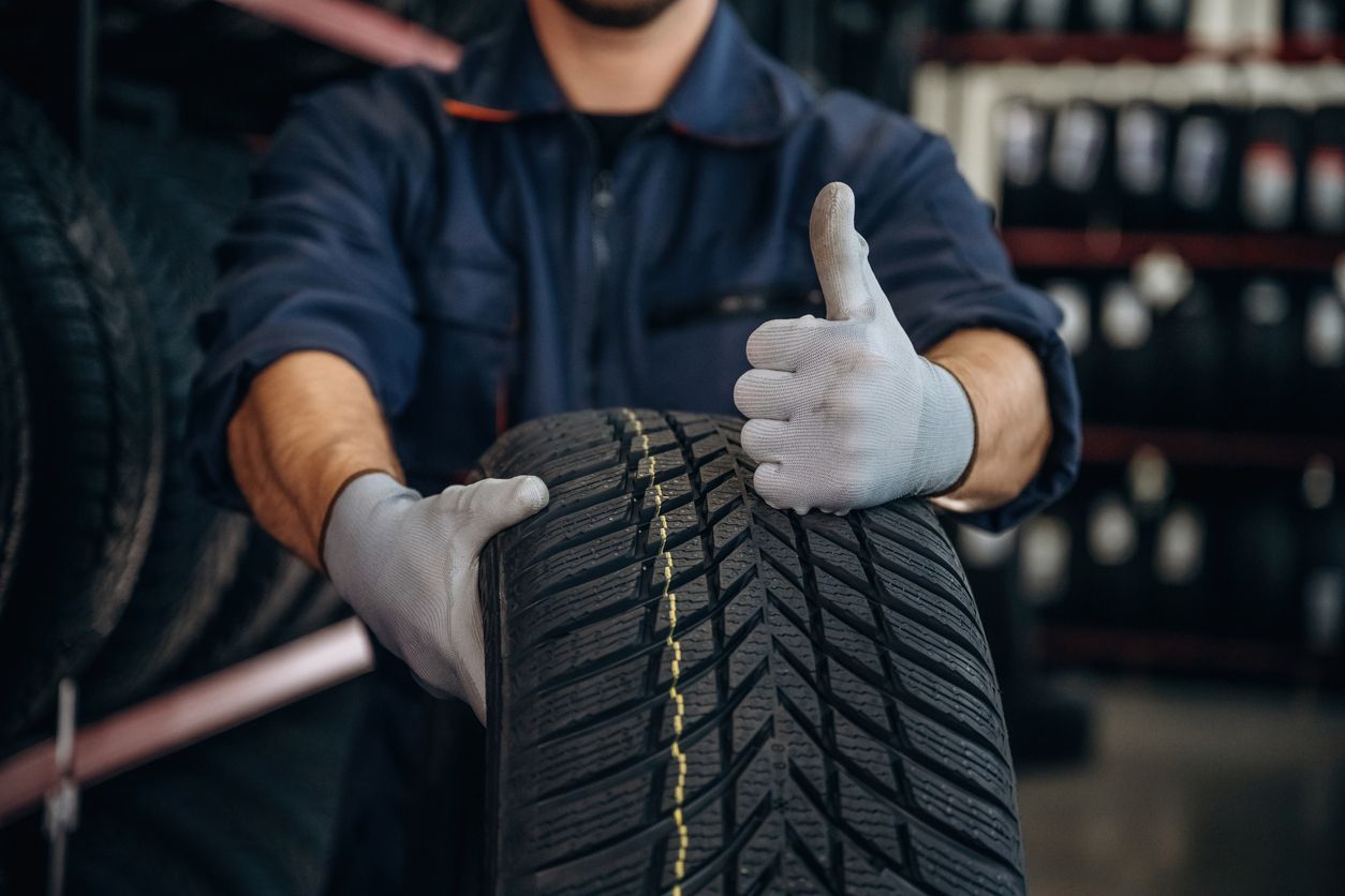 Mechanic holding a new tire and giving a thumbs-up in a garage
