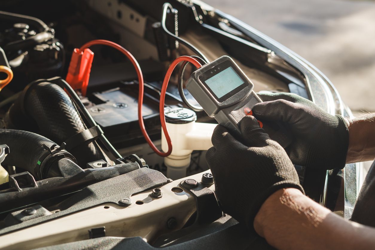Mechanic using a handheld diagnostic scanner on a car engine in an open hood bay