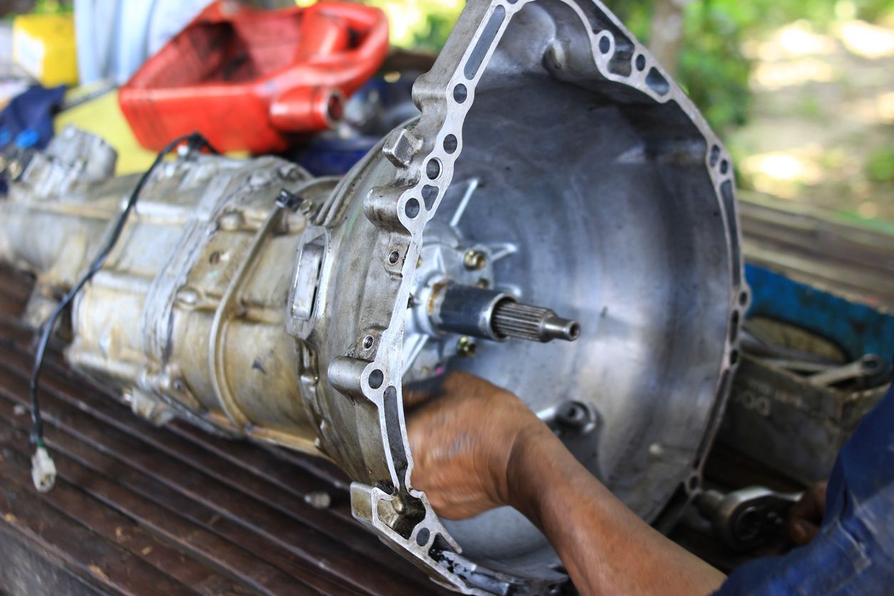 Mechanic working on a car transmission with tools in an outdoor repair area