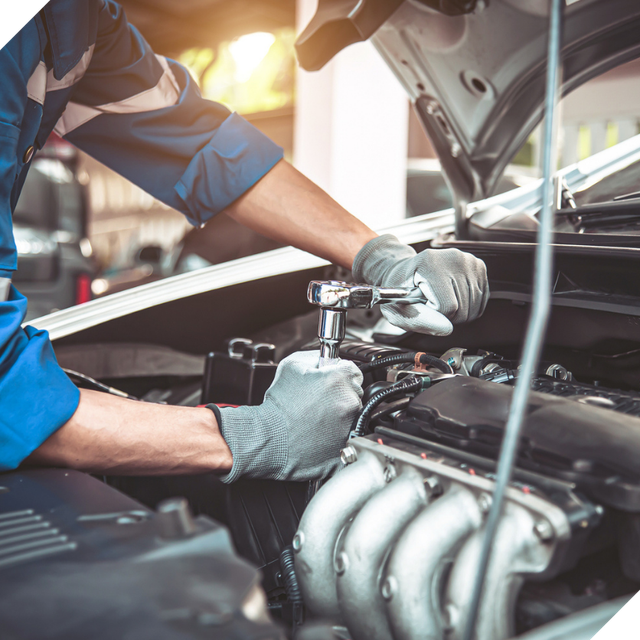 Mechanic in blue uniform working on a car engine in a garage with the hood open