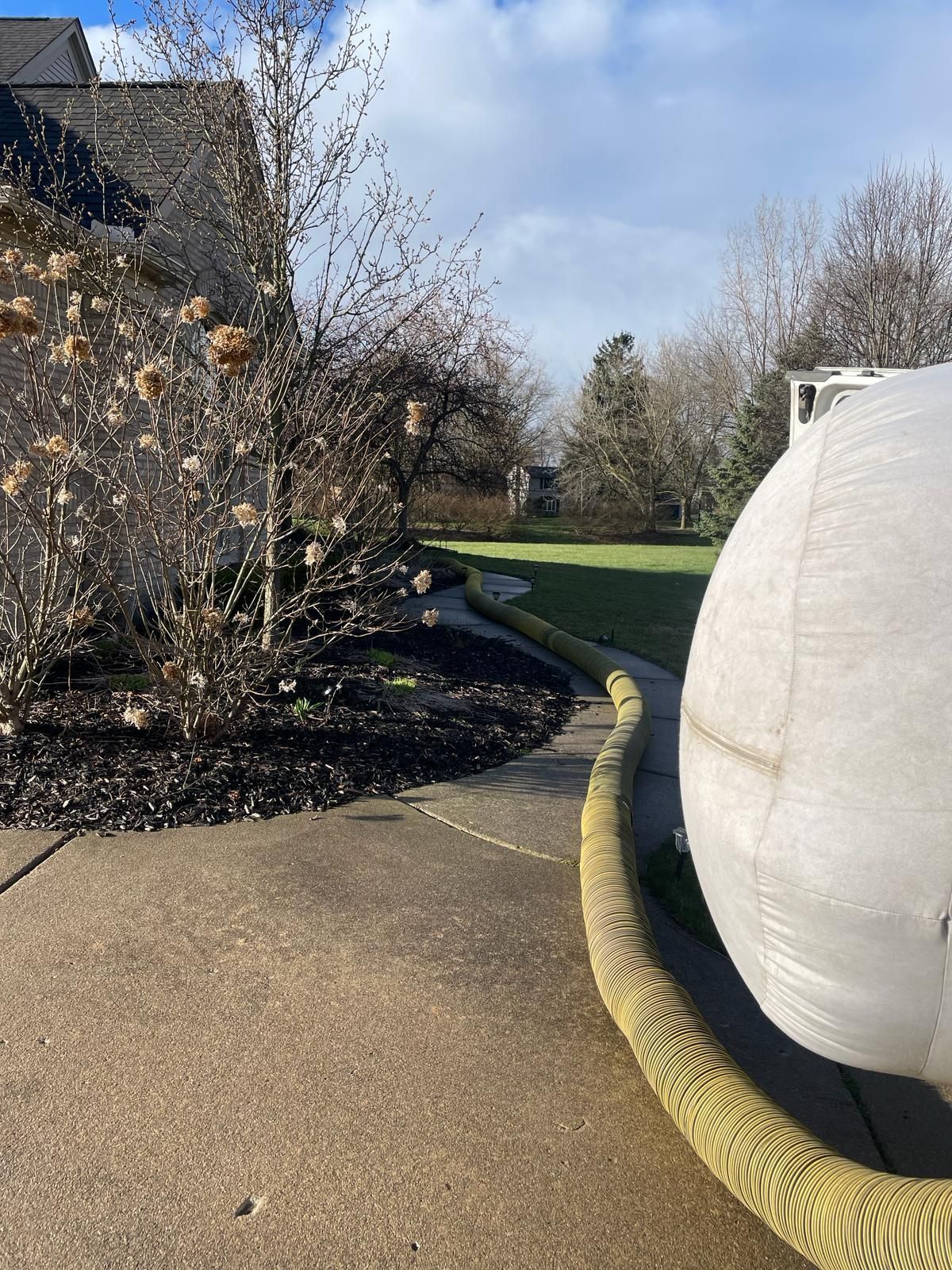 Concrete path with a long yellow hose beside a large white inflatable structure next to a house and landscaping.