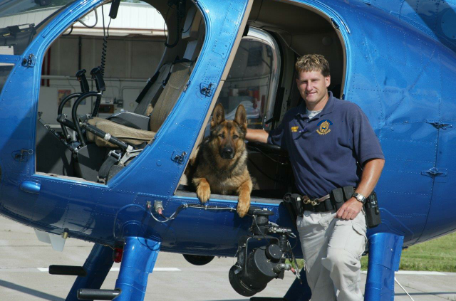 A man standing next to a blue helicopter with a dog on the door