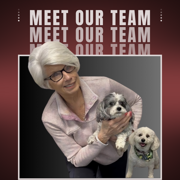 Woman holding two small dogs in front of a “Meet Our Team” sign