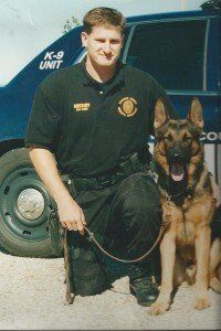 A man kneeling next to a german shepherd in front of a k-9 unit car