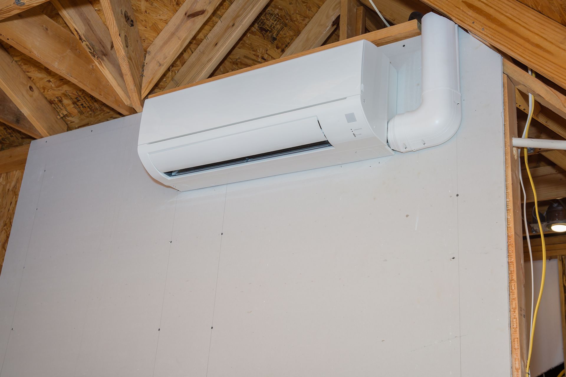 A white air conditioner is hanging from the ceiling of a building under construction.
