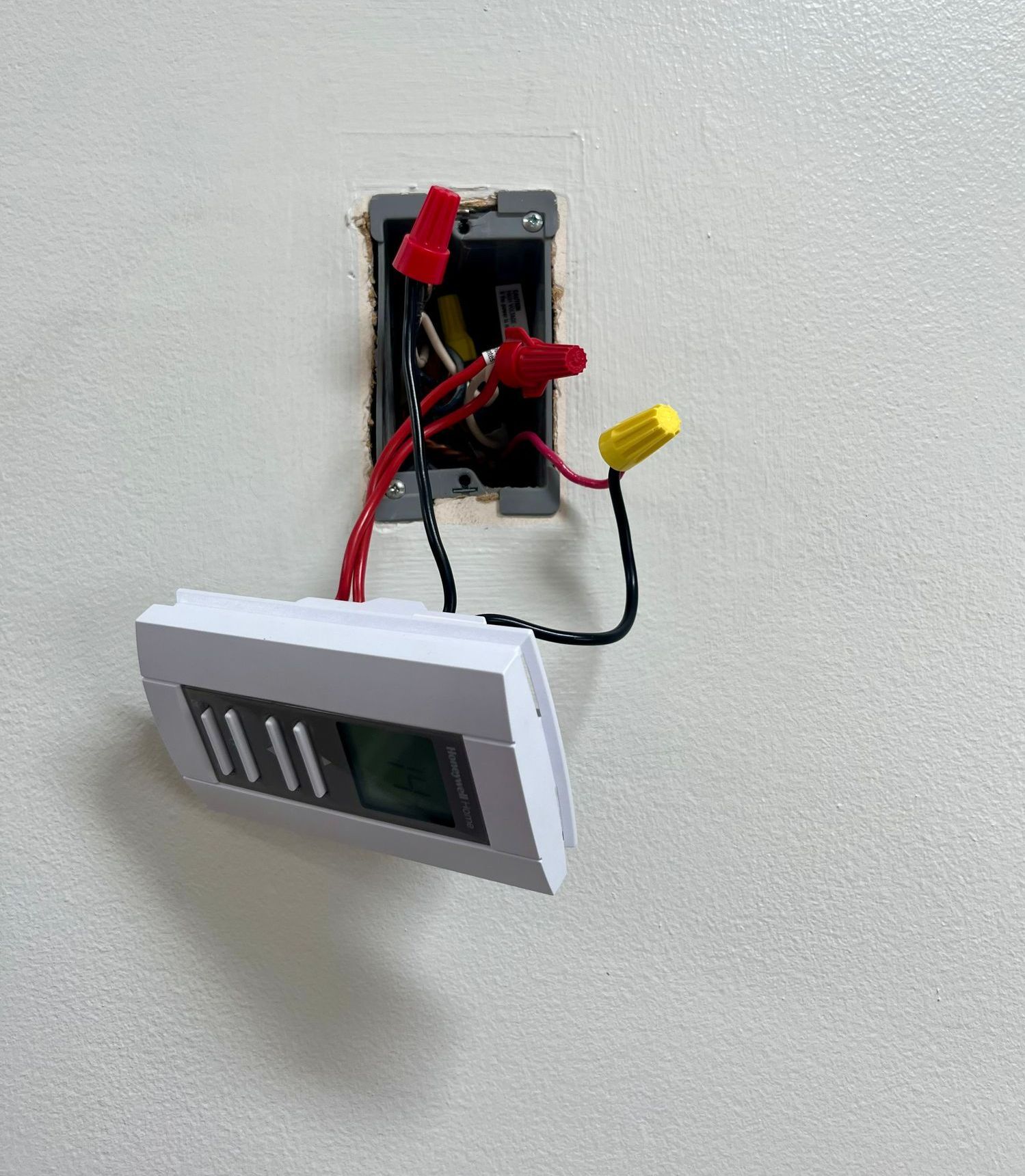 A thermostat is hanging on a wall with wires coming out of it.