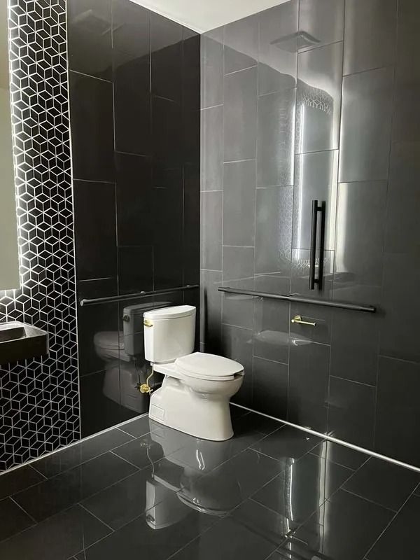 Modern black-tiled bathroom with toilet, glass shower door, and glossy floor