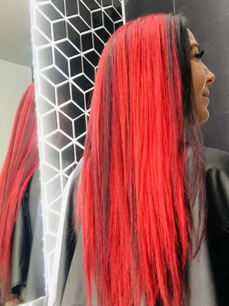 Woman with long red-and-black hair standing by a geometric-patterned wall mirror