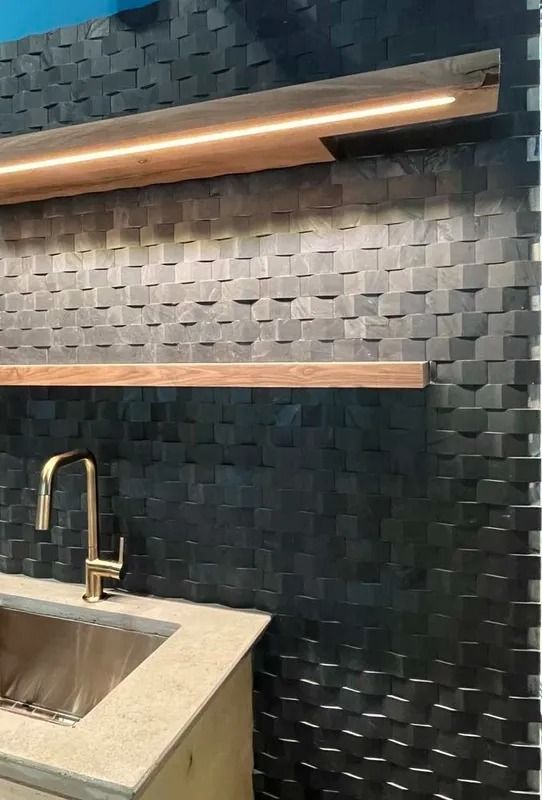 Modern kitchen with dark textured tile wall, floating shelves, and a brass faucet over a sink