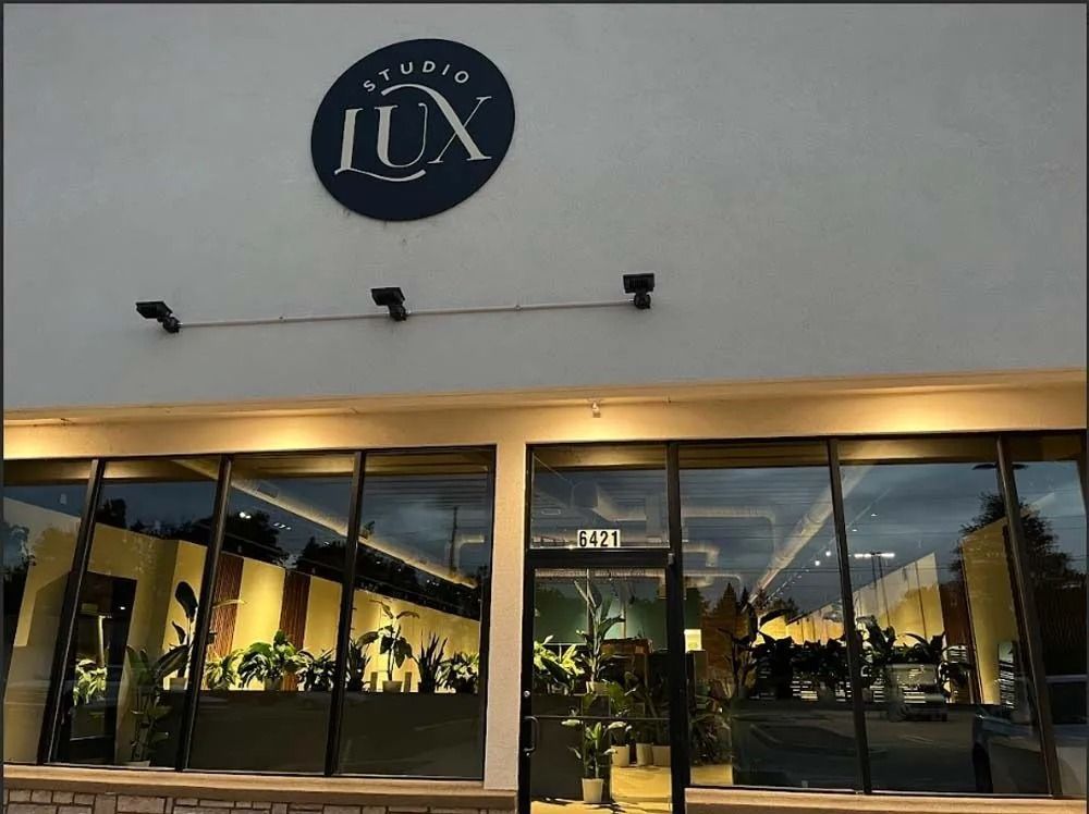 Storefront with large glass windows and a round “LUX” sign above the entrance at dusk