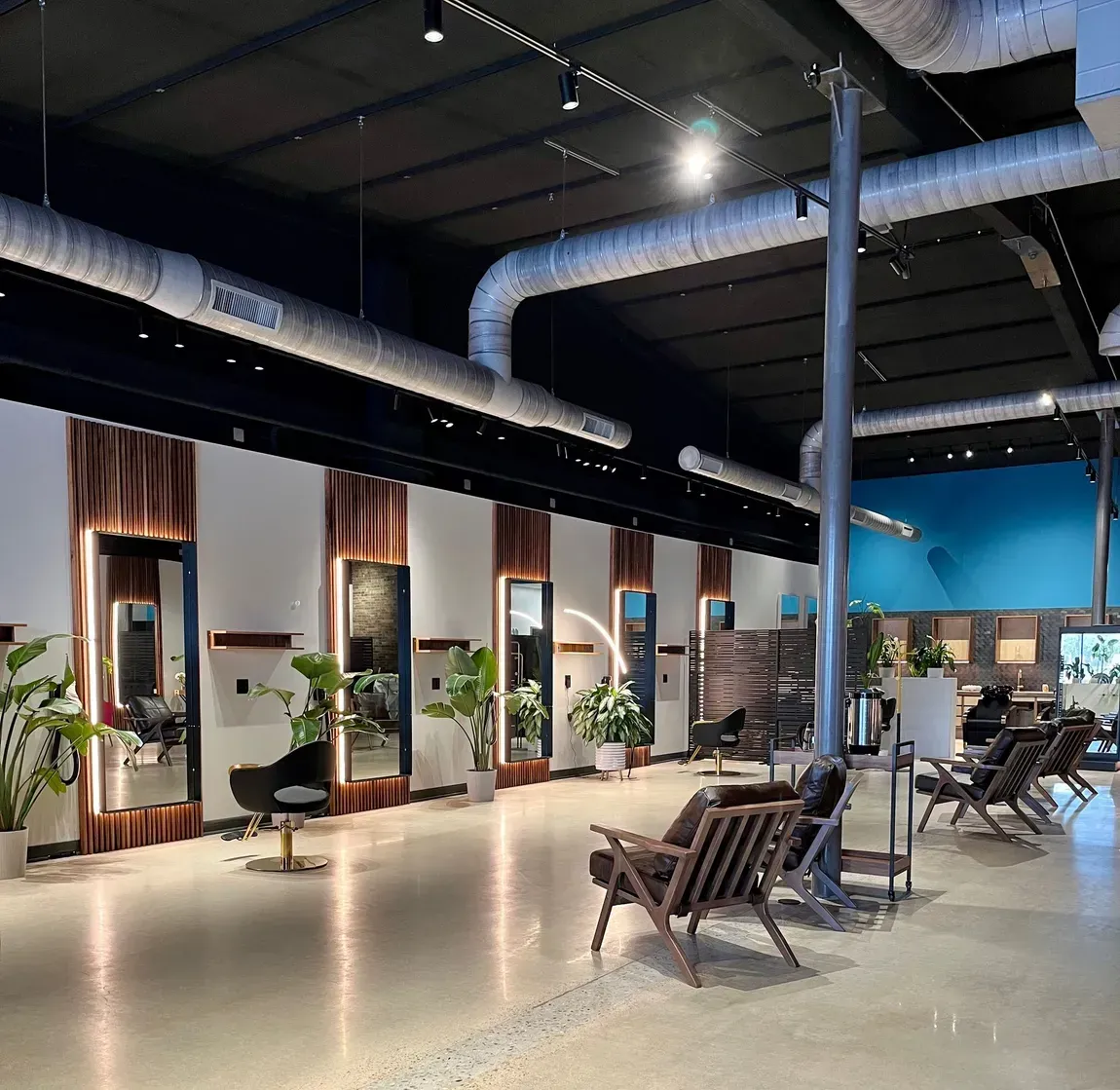 Modern open-plan lounge with lounge chairs, plants, and exposed industrial ceiling lighting