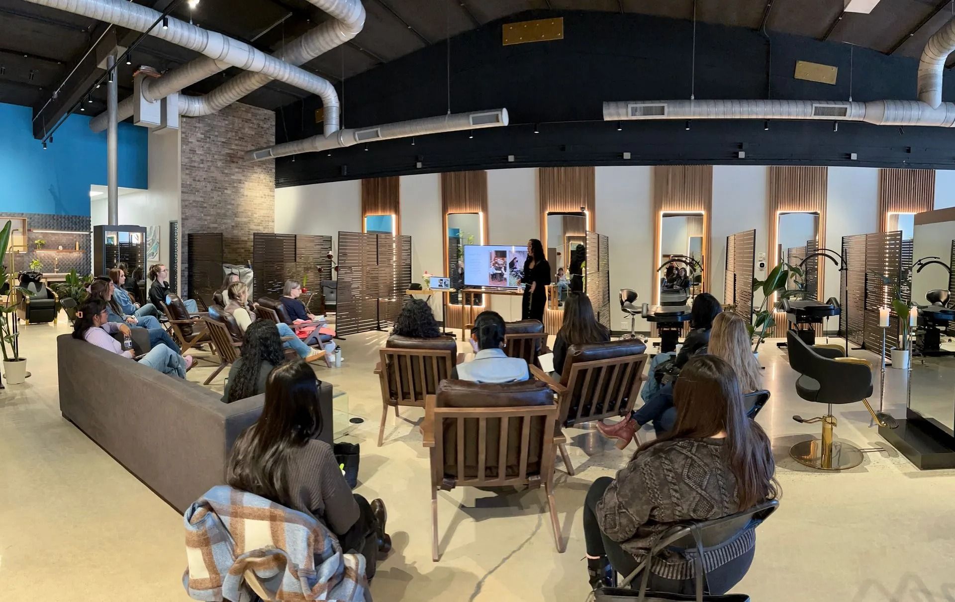 Salon interior with people seated for a presentation and styling stations in the background