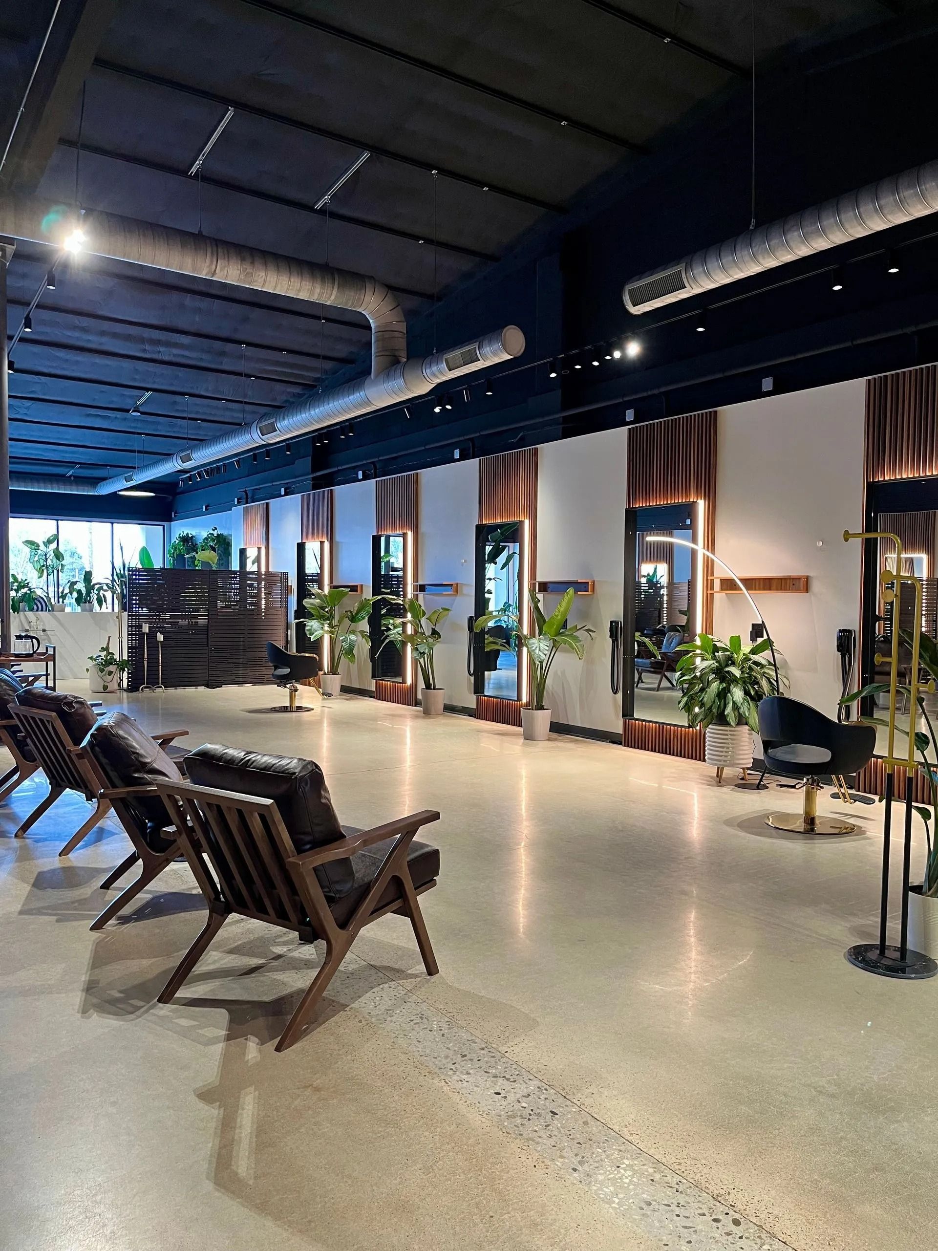 Modern outdoor lounge with wooden chairs, potted plants, and a dark ceiling under warm lighting.