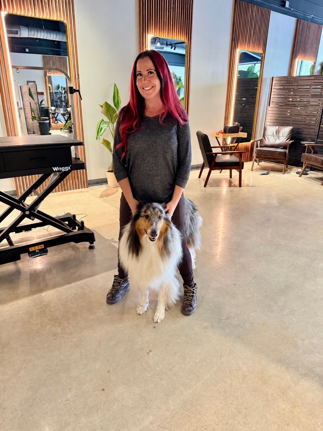 Woman sits with a dog on a leather couch in a dim, cozy lounge with warm lighting and plants.
