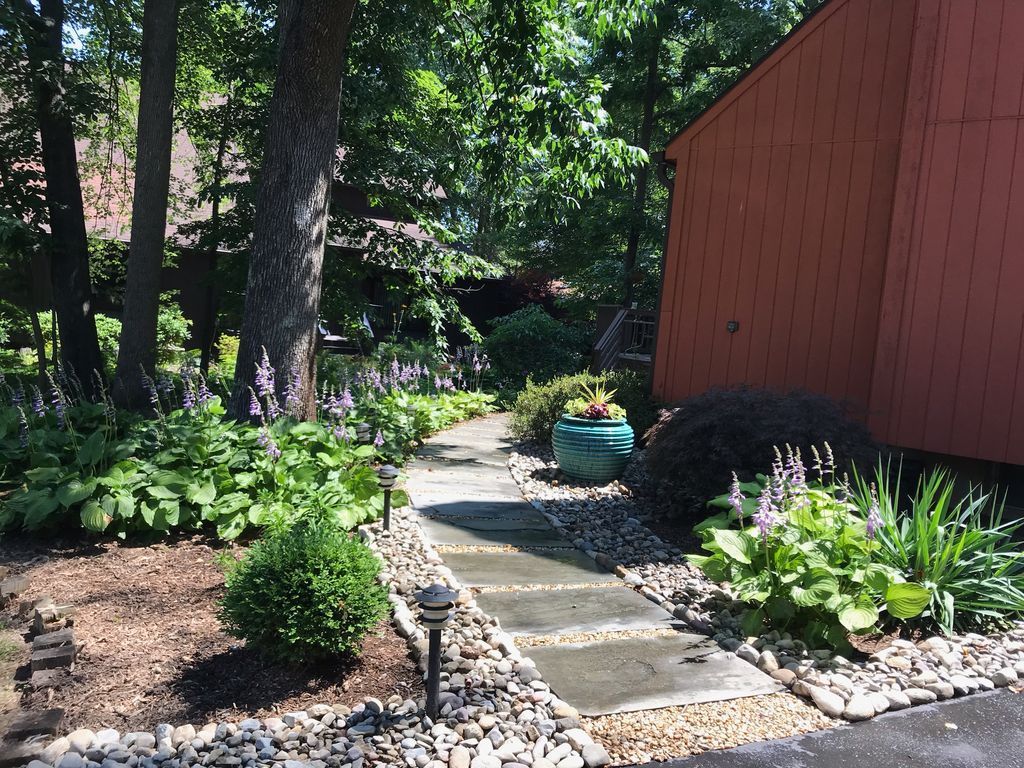 Wooded garden path beside a red shed, with potted plants and stone edging