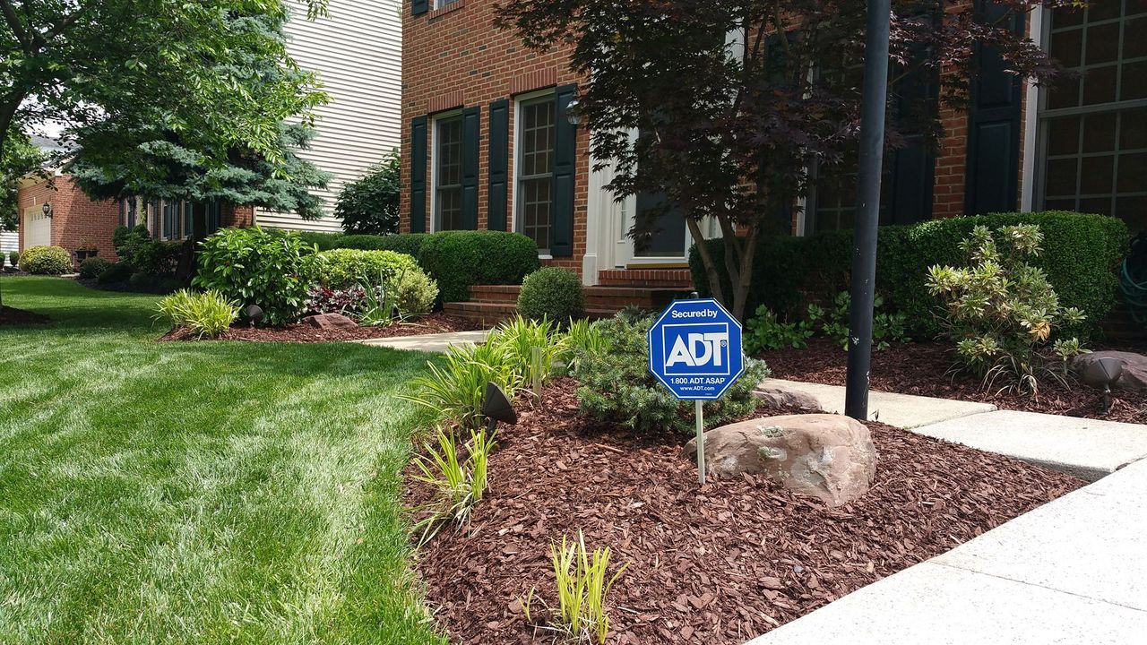 Front yard landscaping beside brick home with an ADT security sign and shrubs