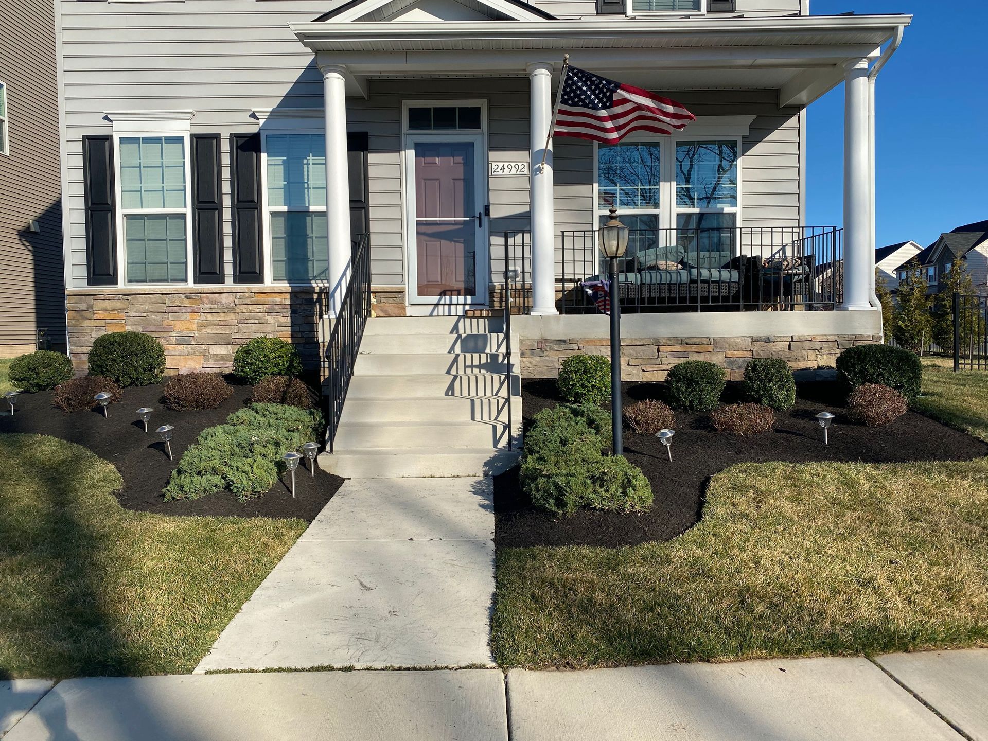Suburban house with front porch, American flag, and concrete walkway leading to the entrance.