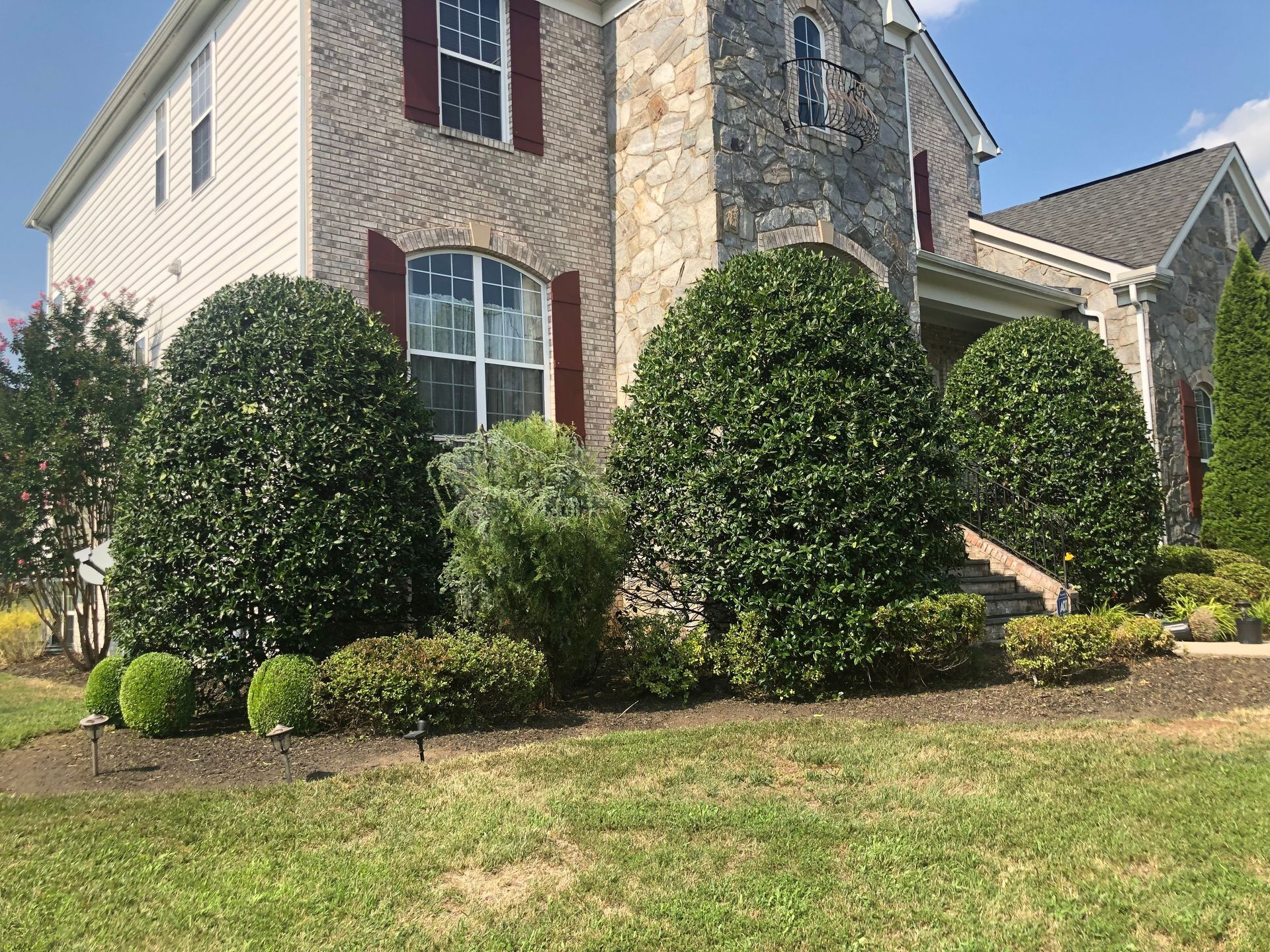 Suburban brick house with manicured shrubs and a stone chimney under a clear sky