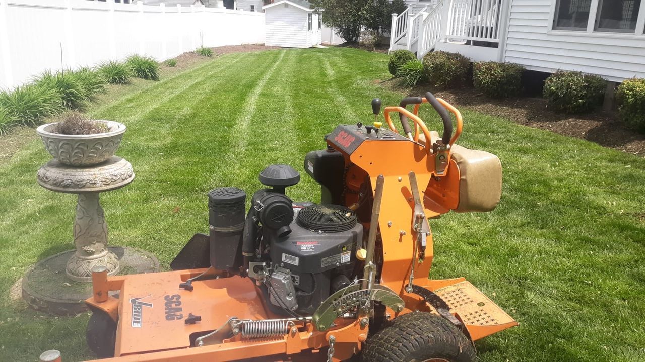Orange lawn mower on a grassy yard beside a white fence and birdbath