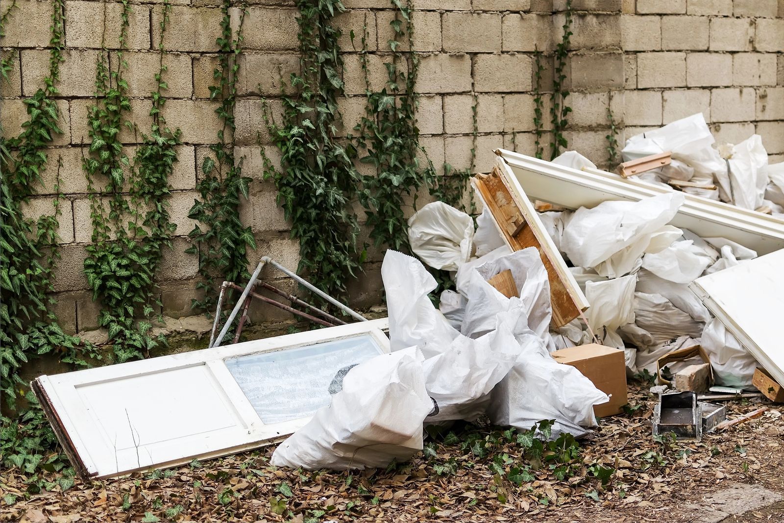 Pile of white debris and broken panels beside a vine-covered brick wall.