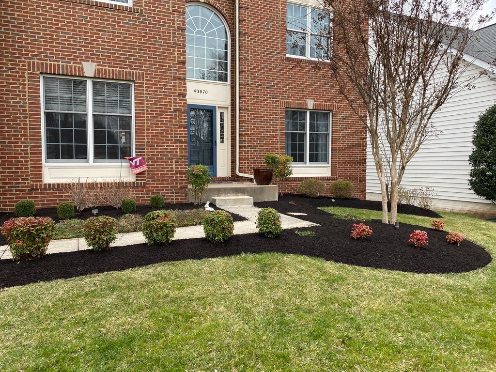 Front yard landscaping with brick house, flower beds, shrubs, and a small tree