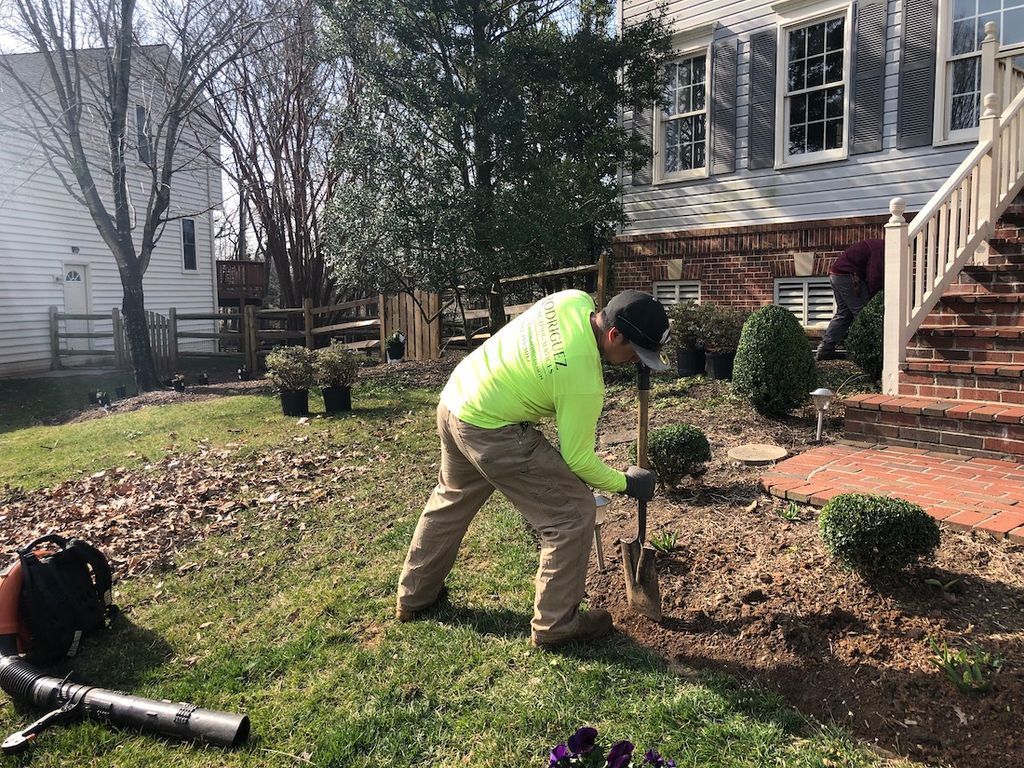 Worker in neon jacket trimming shrubs in a front yard beside a brick house