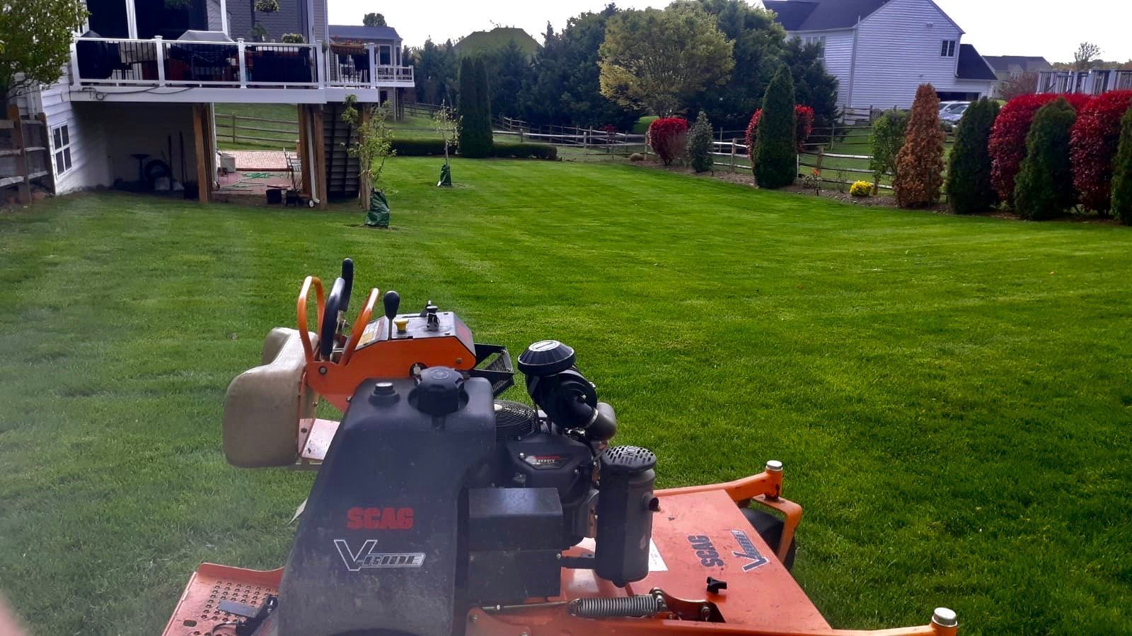 Lawn mower in a lush backyard facing a green lawn with trees and houses in the background