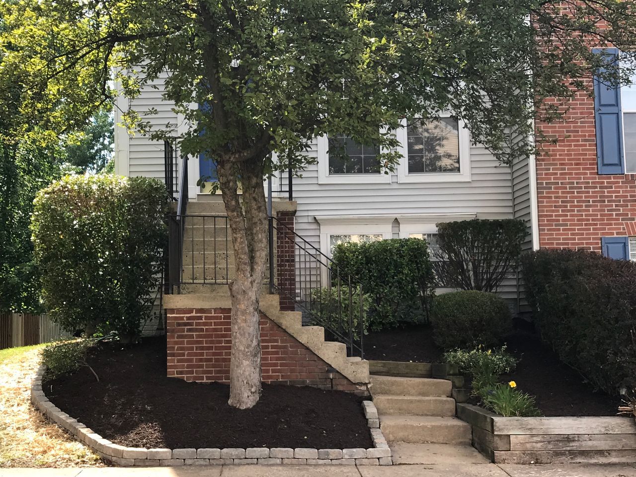 Suburban house front with stone steps, brick accents, shrubs, and a tree in the yard