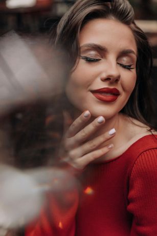 Woman with closed eyes, red lipstick, and sparkly eye makeup in a red sweater.