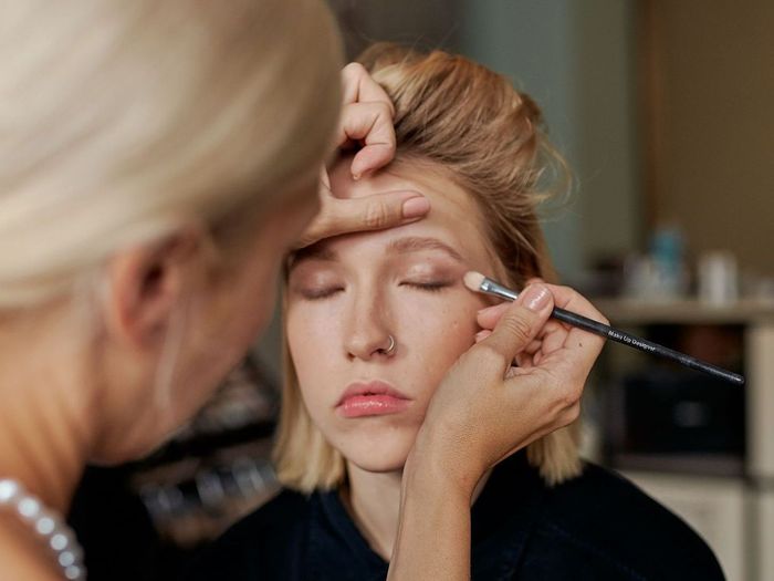 Makeup artist applying eyeshadow to a model’s closed eyelid in a studio setting