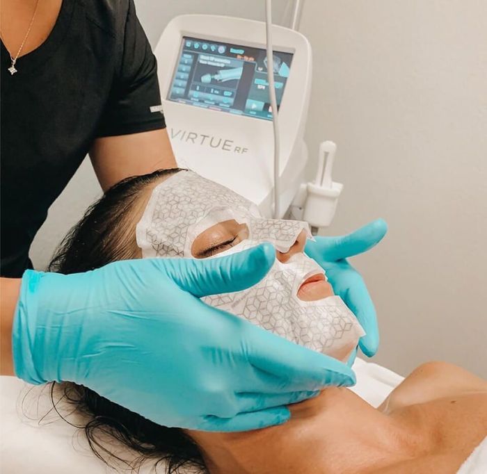 Aesthetic facial treatment with gloved hands applying a white mask to a client in a spa clinic