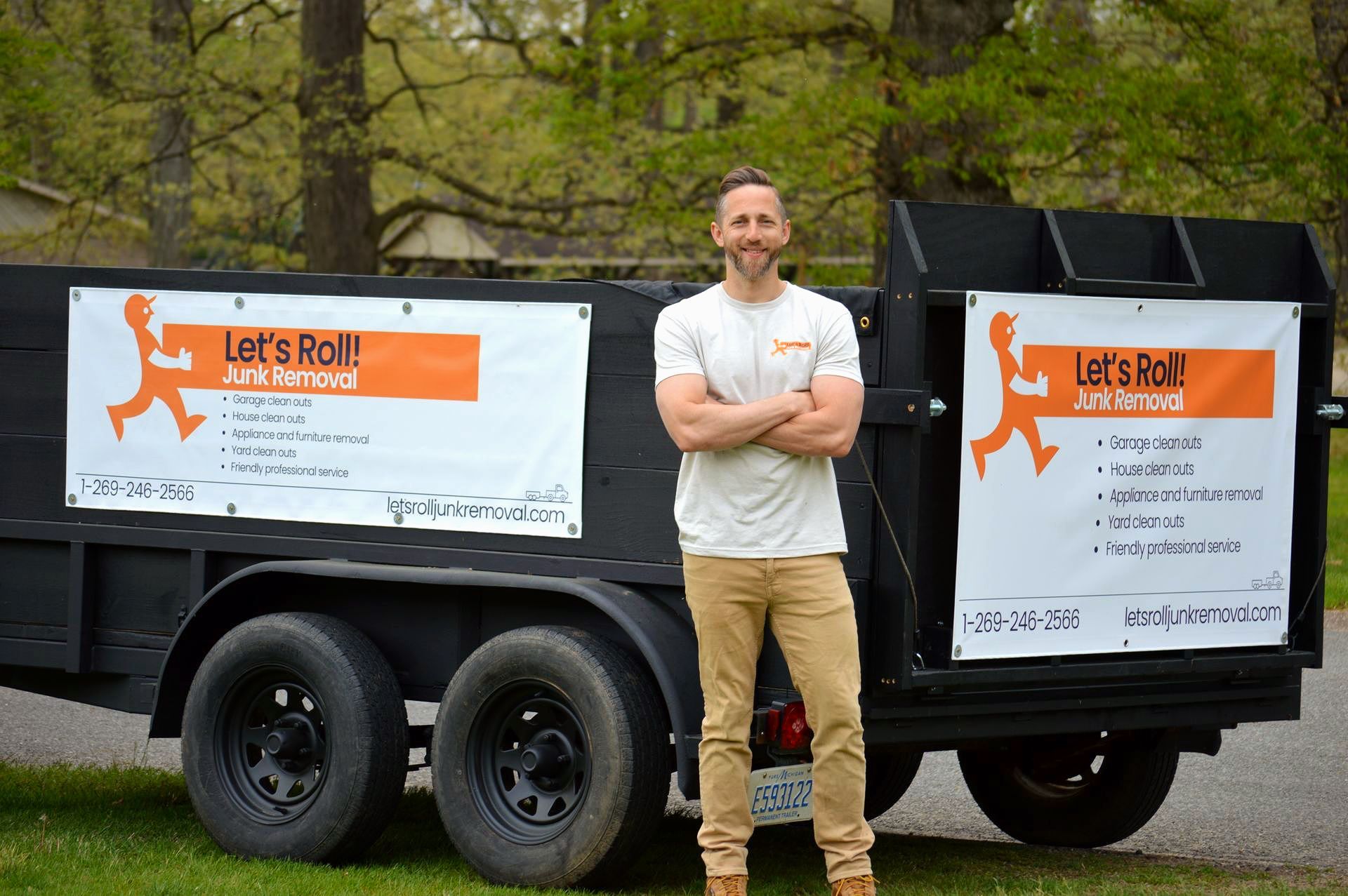 The oner of  Let's Roll Junk removal is standing in front of a dumpster that says let 's roll.